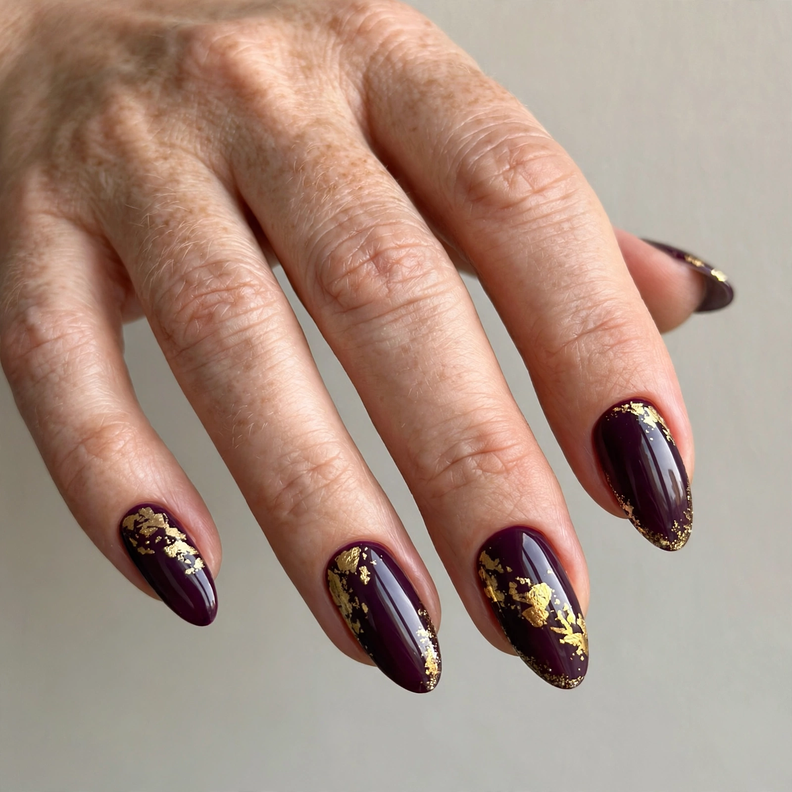 Deep plum manicure with gold leaf foil accents