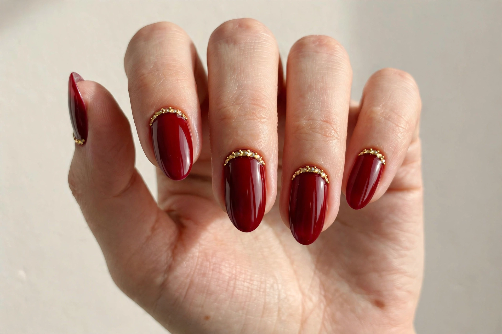 Deep red nails with gold rhinestone crystals along the cuticle line