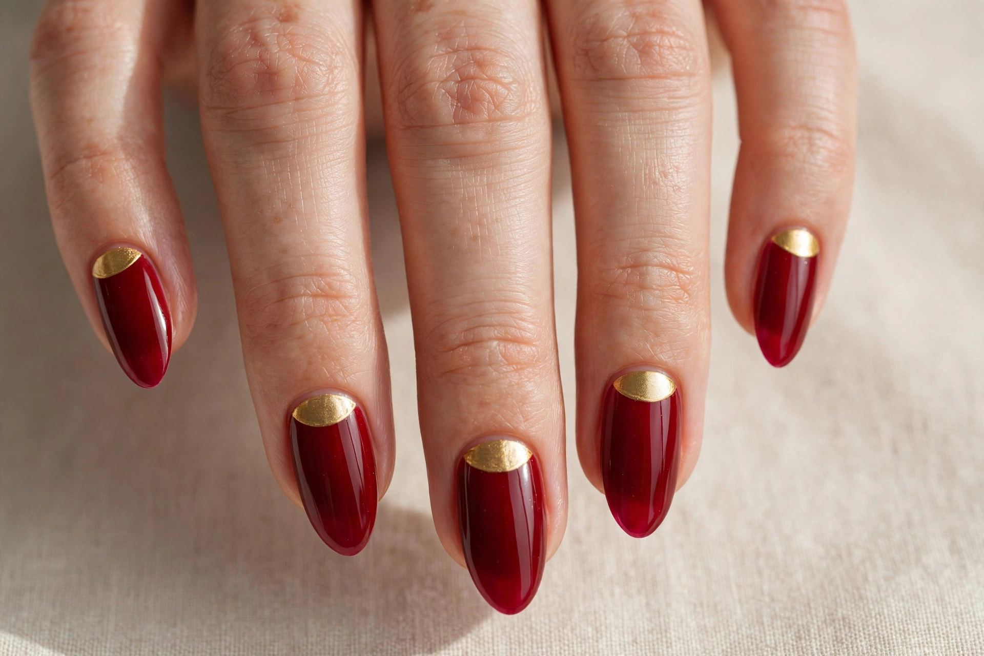 Deep red nails with gold half-moon designs at the base