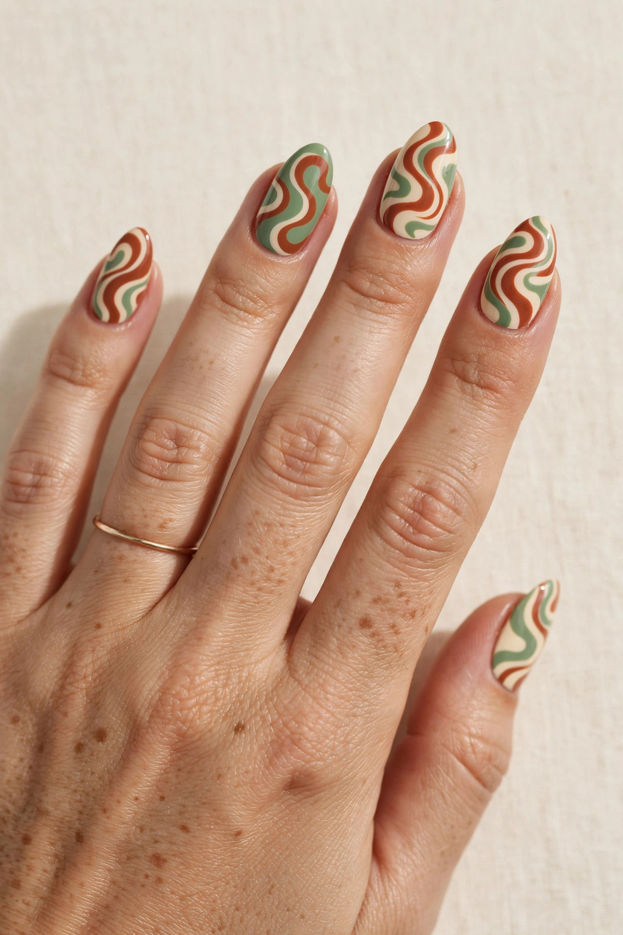 Retro 70s swirl nail art in terracotta, cream and sage green wavy lines