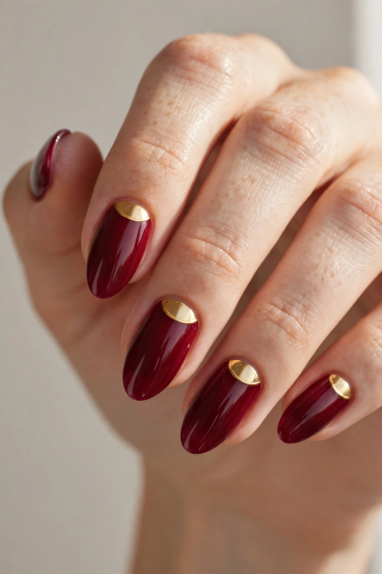 Cranberry nails with a gold half-moon detail at the cuticle