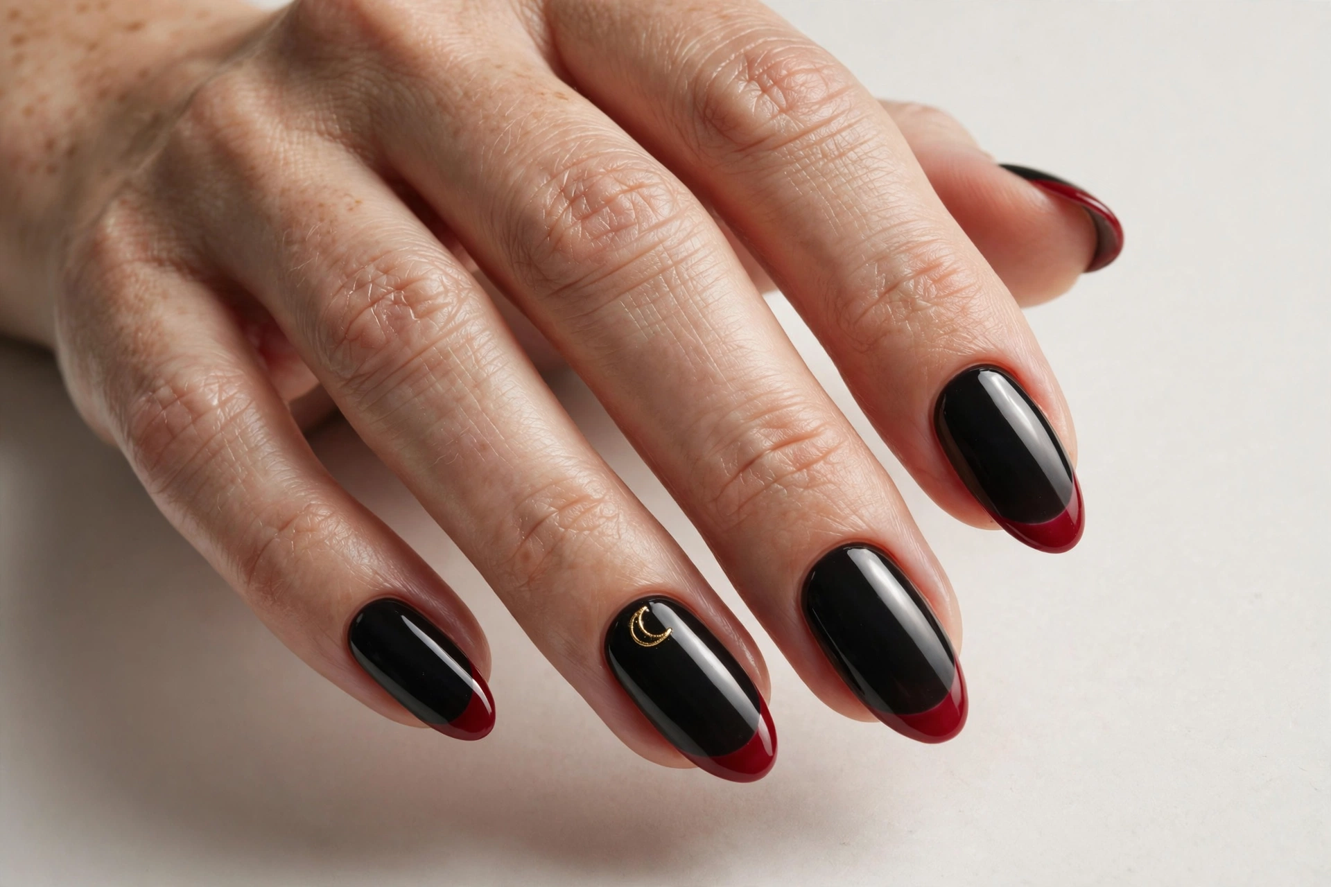 Blood-red French tips over a black base with a small gold crescent moon accent