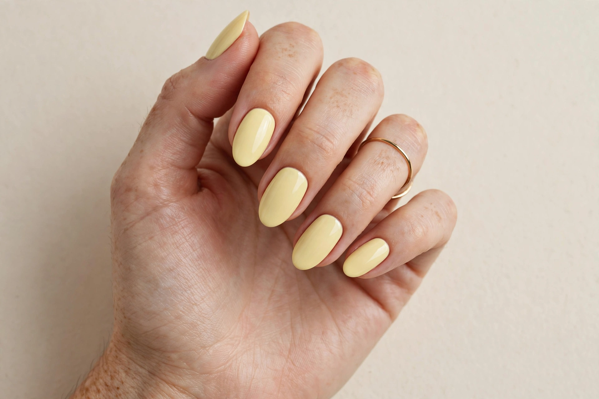 Close-up of a woman's hand with soft butter yellow cream manicure on almond nails