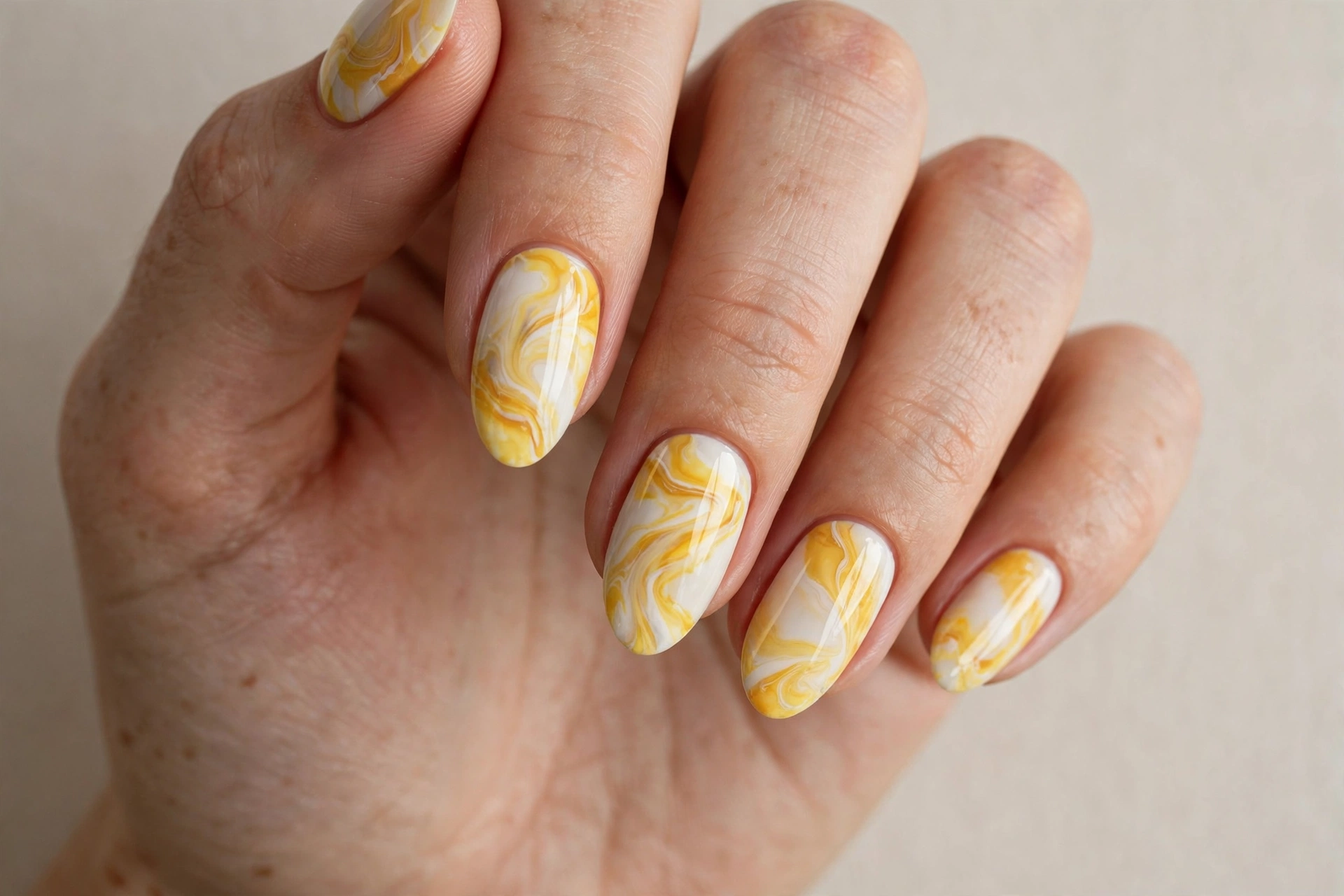 Close-up of a woman's hand with yellow and white marble swirl nail art on almond nails