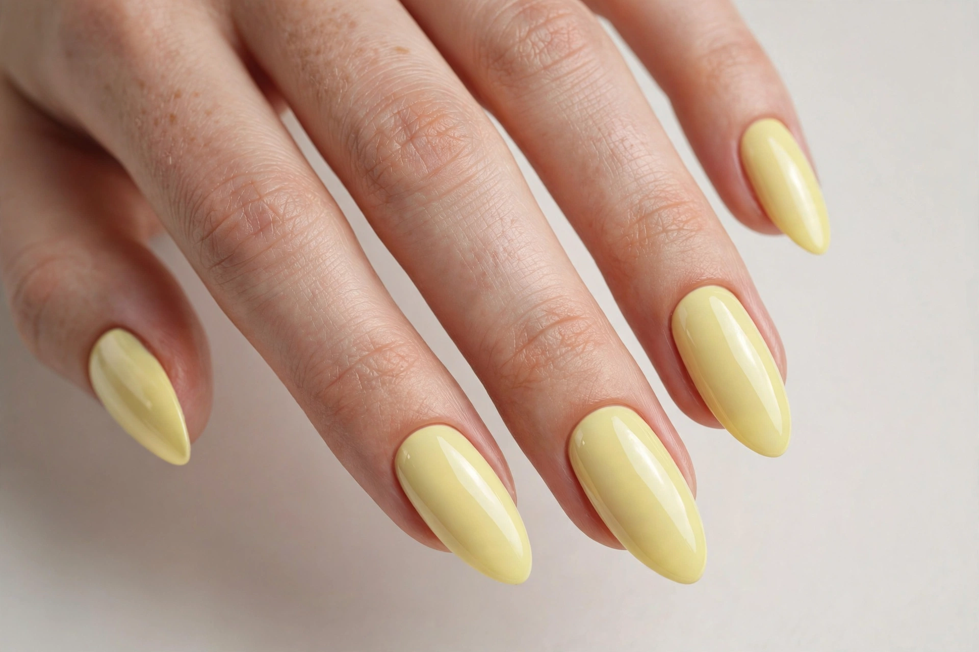Close-up of a woman's hand with pastel yellow glossy manicure on almond nails