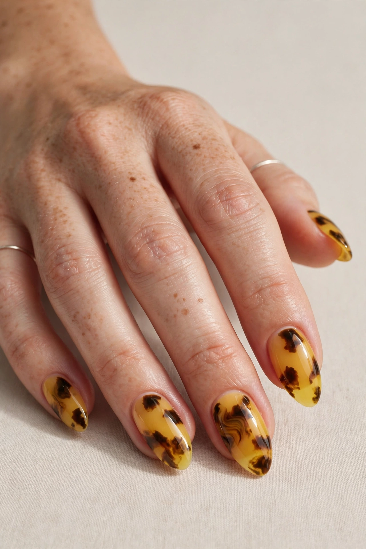 Close-up of a woman's hand with yellow tortoiseshell nail art on almond nails